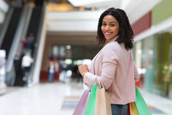 Shoppinghelgen. Leende svart kvinna går i varuhuset med papperspåsar — Stockfoto