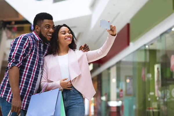 Pareja africana feliz tomando selfie en tienda del departamento después de compras acertadas —  Fotos de Stock
