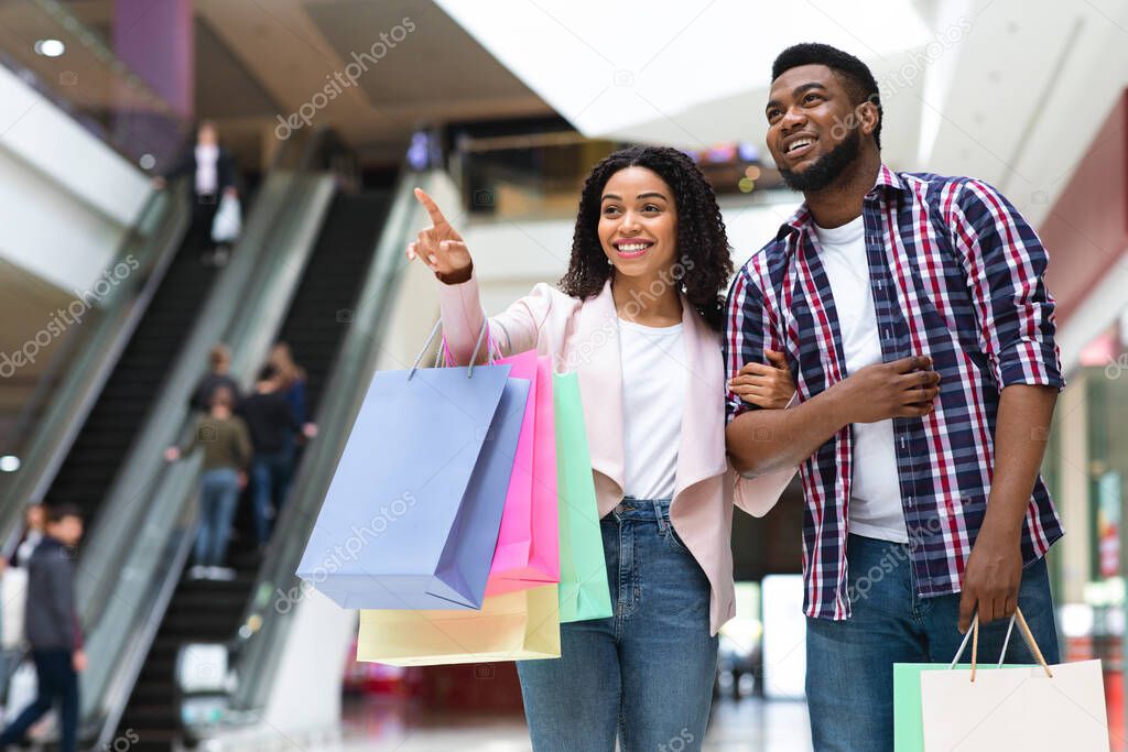 Shopping Together. Black Woman Pointing At Something In Mall, Showing To Boyfriend