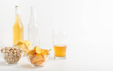 Atıştırmalık ve bira. Cips, fıstık ve nachos tabakta, yarım bardak bira, dolu şişe ve boş şişe.