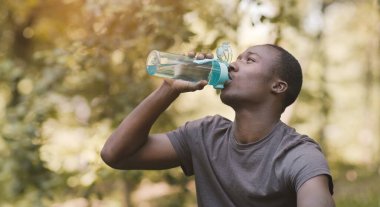 Young black man drinking water from sport bottle at park clipart
