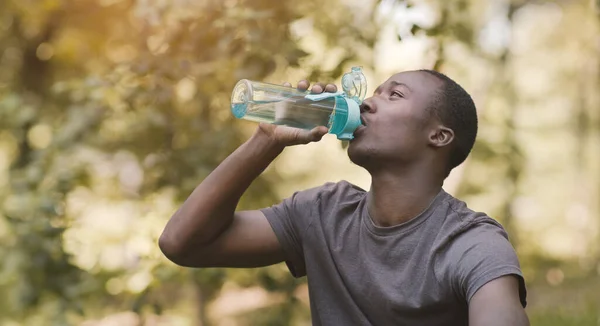 Joven negro bebiendo agua de la botella de deporte en el parque —  Fotos de Stock