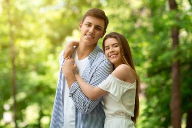 Sevecen kız yazın parkta sevgilisine sarılıyor.