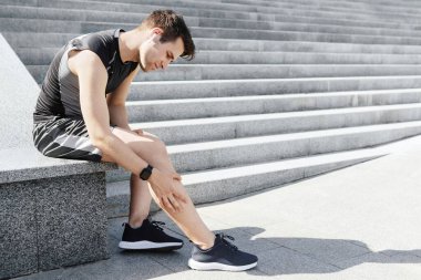 Bacak yaralanması. Yüzünde acı ifadesi olan adam oturur ve bacağını ovar.