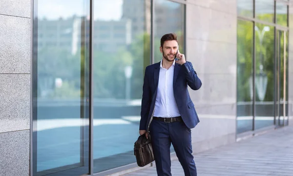Bonito executivo corporativo falando no celular enquanto caminha para seu prédio de escritórios no centro da cidade, espaço de cópia — Fotografia de Stock