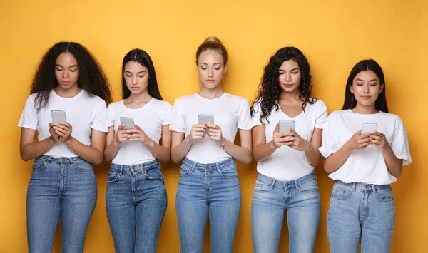 Diverse Girls Using Smartphones Texting Standing Over Yellow Background — Stock Photo, Image