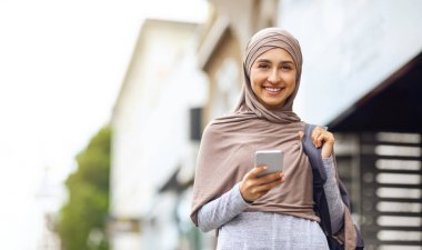 Neşeli bir Arap kadın caddede yürüyor, telefonla.