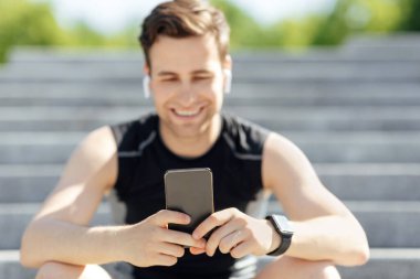 Alet edevatlı modern spor. Kulaklıklı, akıllı saati ve akıllı telefonu olan adam merdivenlerde oturur.