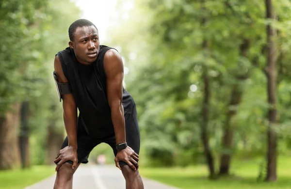 Vyčerpaný africký sportovec odpočívající přes rozmazané park pozadí — Stock fotografie