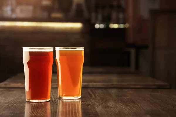 Bright barley beer in pub. Glasses of drink on wooden table in interior