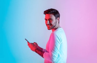 Gençler için cihazlar. Kablosuz kulaklıklı ve ışıklı akıllı telefonlu gülümseyen adam.