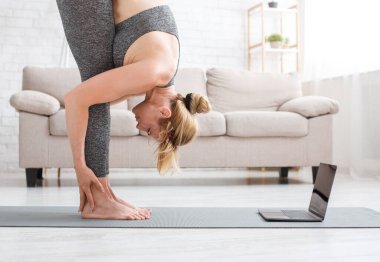 Fitness, yoga ve esneme. Spor kıyafetli bir kadın dizüstü bilgisayarla mindere kıvrılıyor.