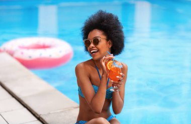 Dışarıda bikinili, bikinili, nefis bir kokteyl içen siyah bir kadın var.