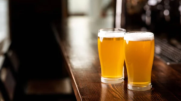 Salidas con amigos en pub y cerveza. Dos vasos de cerveza ligera con espuma en el mostrador de bar de madera a la luz del día en el interior del pub —  Fotos de Stock
