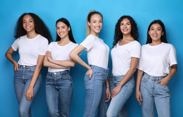 Meninas muito multiculturais sorrindo em pé no fundo do estúdio azul — Fotografia de Stock