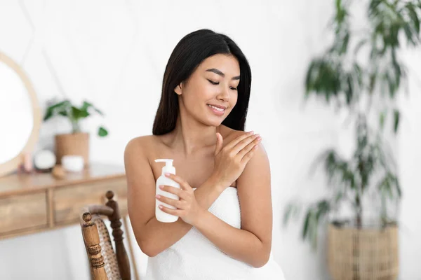 Smiling asian girl applying body lotion on her skin — Stok Foto