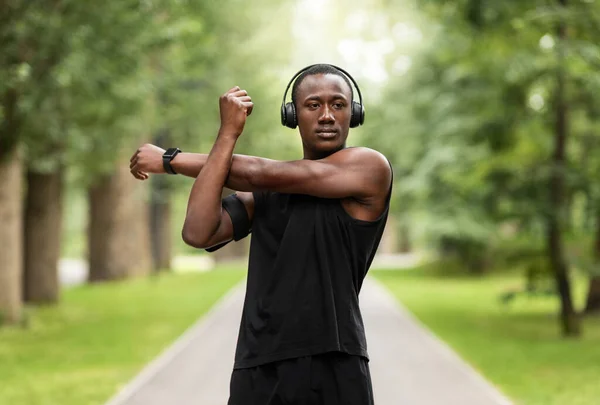 Konzentrierter afrikanischer Sportler streckt die Arme aus, trainiert im Park — Stockfoto