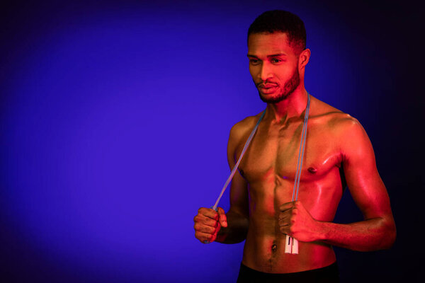 Workout Motivation. Black Muscular Man Holding Jump Rope Looking Aside Posing On Blue Background. Studio Shot, Free Space