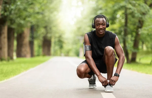 Alegre africano chico atando cordones en sus zapatillas antes de entrenar — Foto de Stock