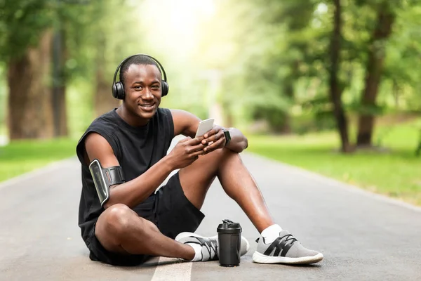 Gioioso sportivo africano che si riposa sulla pista da jogging al parco — Foto Stock