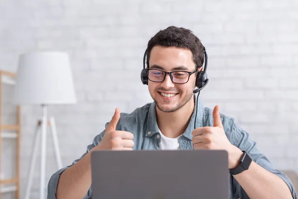 Lächelnder Typ mit Brille zeigt mit erhobenem Zeigefinger auf Laptop im Wohnzimmer — Stockfoto