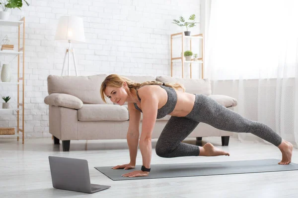 Fitnesstraining der sportlichen Frau. Übungen für Beine auf Matte mit Laptop im Wohnzimmer — Stockfoto