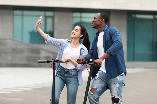 Para jeżdżąca na zmotoryzowanych hulajnogach, robiąca selfie — Zdjęcie stockowe