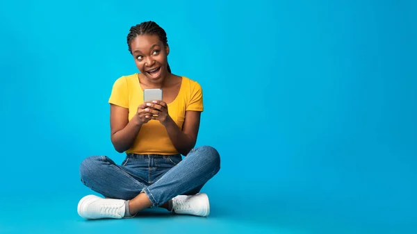 青い背景の上に座っているスマートフォンを使用して肯定的なアフリカの女の子,パノラマ — ストック写真