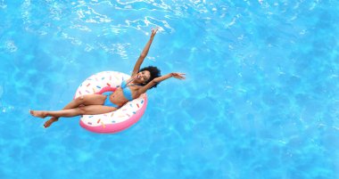 Havuzun üstünde şişme yüzükle yaz güneşinin tadını çıkaran heyecanlı genç bir kadın. Boş boşluk