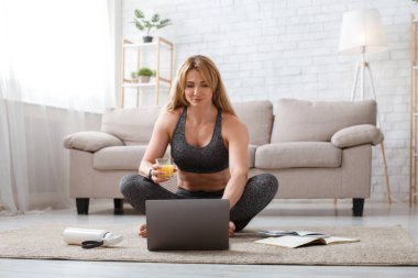 Sağlıklı yaşam tarzı, diyet ve spor. Lotus 'ta oturan kadın elinde meyve suyu bardağıyla dizüstü bilgisayara bakıyor.