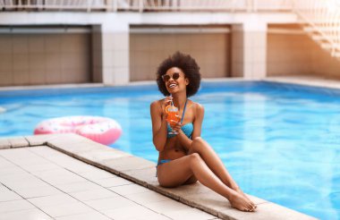 Seksi siyah bayan güneşleniyor ve yaz kokteyli içiyor. Açık havuz, fotokopi odası.