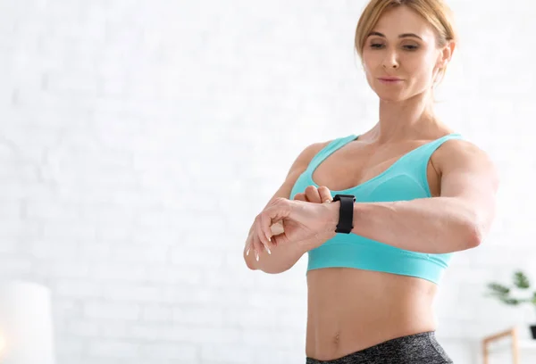 Resultado del entrenamiento. Musculosa mujer adulta en ropa deportiva mira reloj inteligente —  Fotos de Stock