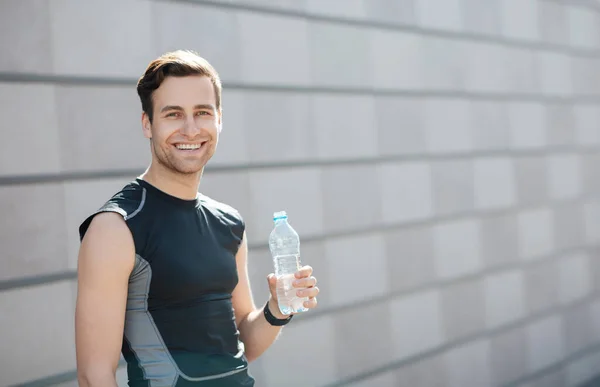 Agua para entrenar en la ciudad. Sonriente chico en ropa deportiva sostiene botella —  Fotos de Stock