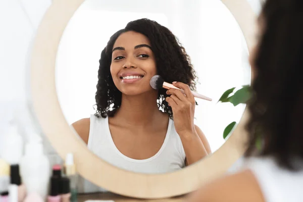 Mujer negra hermosa feliz aplicando el polvo con el cepillo, haciendo el maquillaje diario — Foto de Stock