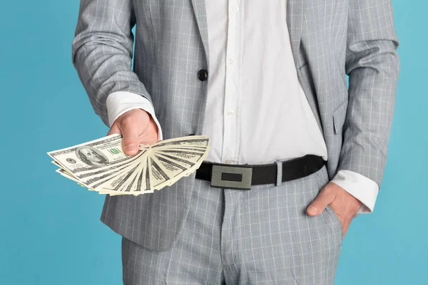 Closeup of young man in business suit showing fan of cash on blue background — Stock Photo, Image