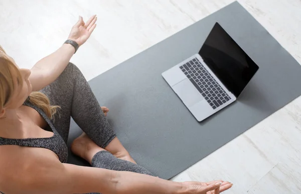 Ejercicio y relajación. Mujer en posición de loto se sienta en la estera en el suelo con el ordenador portátil —  Fotos de Stock