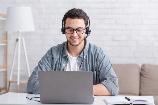 Kundtjänst online hemma. Killen med glasögon och headset, tittar på laptop, sitter vid bordet — Stockfoto