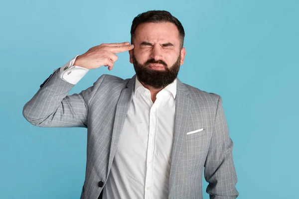 Stressed businessman pointing fingers to his head like gun, wanting to shoot himself on blue background — Stock Photo, Image