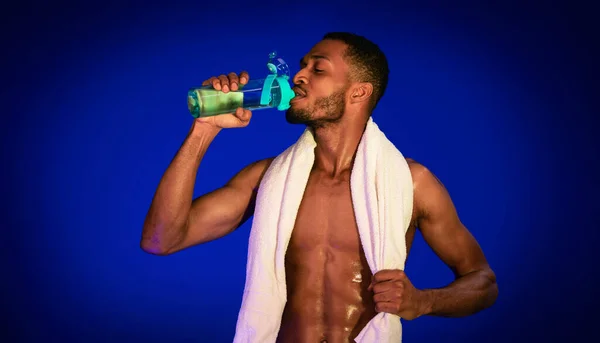 Africano ajuste hombre agua potable de pie en azul estudio fondo — Foto de Stock