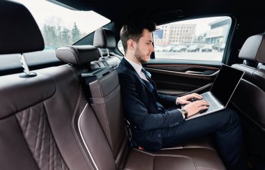 Genç işadamı dizüstü bilgisayarını lüks bir arabada kullanıyor.