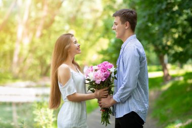 Romantik milenyum adamı, parkta sevgilisine bir buket güzel çiçek sunuyor.