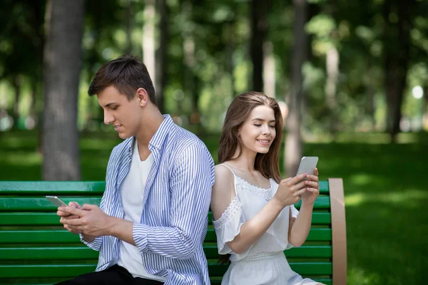 Gadget addiction. Millennial couple busy with smartphones, talking to virtual friends and ignoring each other at park — Stock Photo, Image