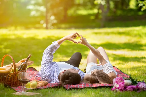 Casal afetuoso fazendo coração com as mãos durante piquenique no parque no verão — Fotografia de Stock