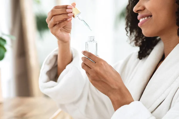 Tratamiento de belleza en casa. Mujer africana sonriente abriendo botella con suero hidratante —  Fotos de Stock