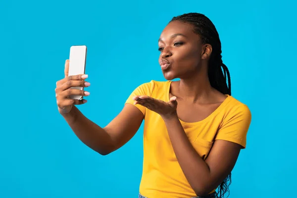 Девушка, использующая телефон для видеозвонков, посылающих воздушные поцелуи, студия — стоковое фото