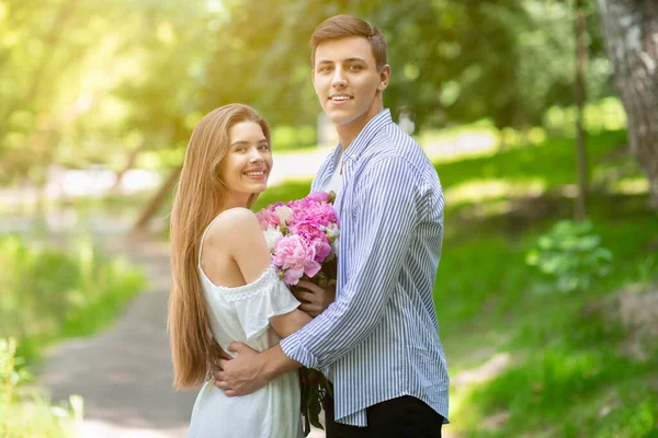 Celebración de cumpleaños. Pareja cariñosa con ramo de preciosas flores de peonía abrazándose en el parque en un día soleado — Foto de Stock