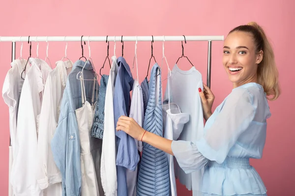 Portrait of cheerful girl choosing clothes standing near rack — Stock Photo, Image