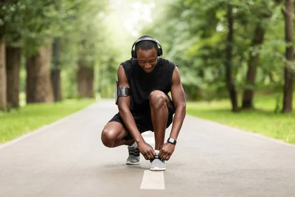 Черный спортсмен завязывает шнурки на дорожке для бега по парку — стоковое фото