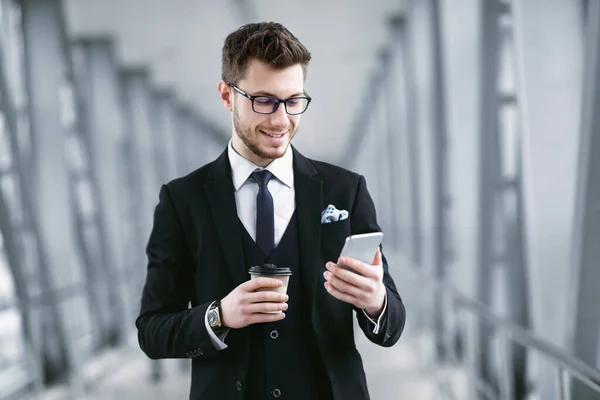 Homem de negócios sorrindo mensagens de texto no telefone celular, beber café — Fotografia de Stock