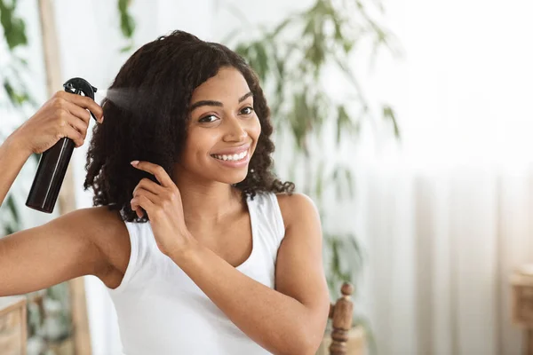 Fryzura. uśmiechnięty czarny kobieta stosując teksturowania Spray do jej piękne kręcone włosy — Zdjęcie stockowe